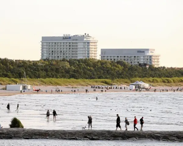 Ludzie spacerują po najszerszej plaży w Polsce, w tle hotele Radisson i Hilton.