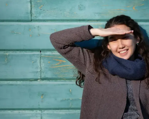 Ragazza sorride, coprendosi gli occhi dal sole. Il fastidio alla luce non le impedisce di godersi la giornata.