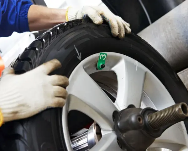Tecnico con guanti esegue equilibratura gomme per eliminare vibrazioni. Ruota su macchinario specifico.