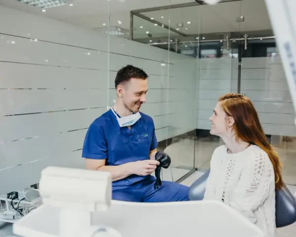 Dentysta w niebieskim uniformie rozmawia z pacjentką, sugerując nowy lek na ból zęba.