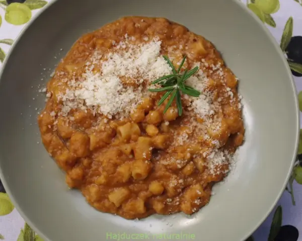 Pyszny makaron z ciecierzycy w sosie pomidorowym, posypany parmezanem i udekorowany gałązką rozmarynu.