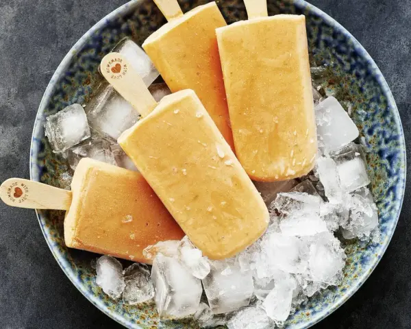 Vier selbstgemachte Papaya-Eis am Stiel liegen auf zerstoßenem Eis in einer blauen Schale.