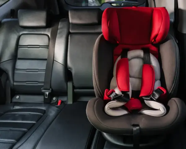 Czerwony fotelik dziecięcy z pasami bezpieczeństwa zamontowany na tylnym siedzeniu samochodu. To właśnie system isofix, co to jest? Bezpieczeństwo przede wszystkim!