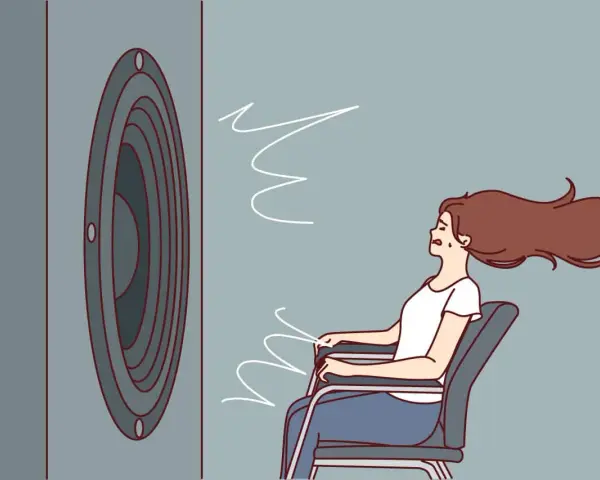 Une femme assise, les cheveux au vent, face à un haut-parleur. Le son est si fort qu'il en devient une force physique, illustrant la définition du décibel.