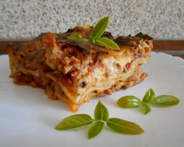 Kawałek pysznej lasagne z mięsem mielonym, udekorowany listkami bazylii. Prosty przepis na domową lasagne.