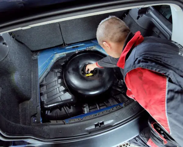 Mechanik sprawdza butlę LPG w bagażniku. Dowiedz się, ile kosztuje legalizacja butli LPG i jakie są formalności.