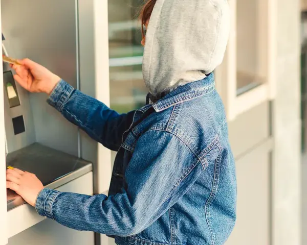 Jugendlicher mit Kapuze und Jeansjacke am Geldautomaten. Ein Beispiel für mögliche Verhaltensauffälligkeiten, die auf Kleptomanie bei Kindern hindeuten könnten.