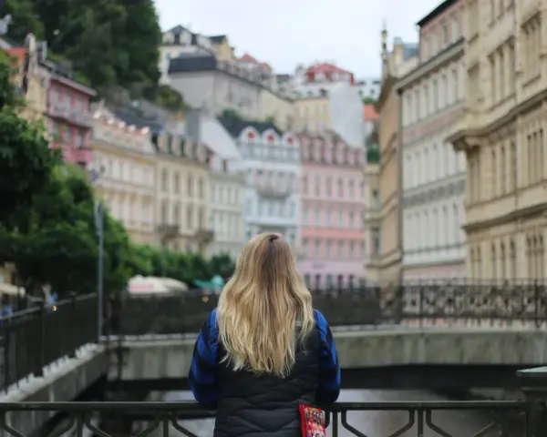 A woman with blonde hair gazes at colorful buildings, perhaps planning her day trips from Prague by train.