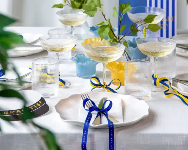 Festligt dukat bord med champagneglas, blå och gula band som knyts i en blå rosett, samt en studentmössa.