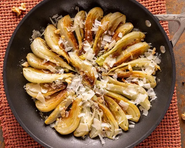 Finocchi in padella dorati e saporiti, guarniti con scaglie di formaggio e noci croccanti.