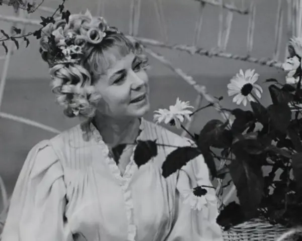 Ilona Stawińska w kwiecistej fryzurze i jasnej sukni, otoczona kwiatami, wygląda jak z baśni.