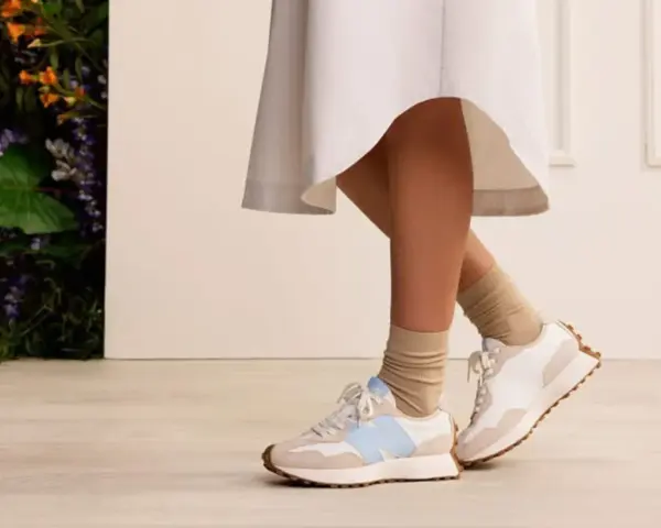 Elegancka sukienka i sportowe buty tworzą stylowy kontrast. Nogi w beżowych skarpetkach i białych sneakersach z błękitnym logo.