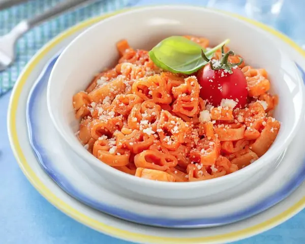 Makaron w kształcie zwierzątek z sosem pomidorowym, posypany parmezanem, udekorowany pomidorkiem i bazylią.