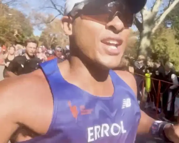 En löpare i blått linne, med texten "ERROL", kämpar på för att springa marathon. Publiken hejar längs banan.