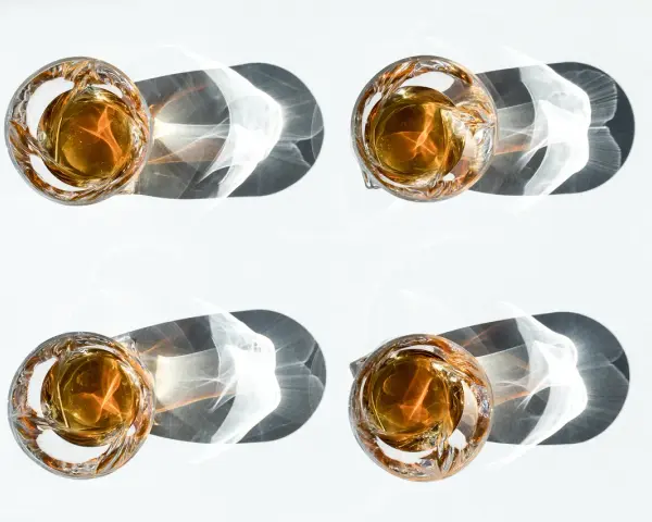 Vier Gläser mit bernsteinfarbenem Whisky werfen dramatische Schatten. Ein visueller Vergleich, der den Unterschied Scotch und Bourbon verdeutlicht.