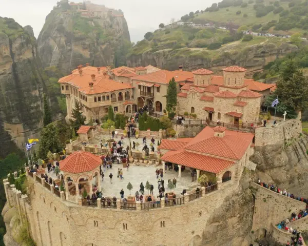 A stunning view of the monasteries of Meteora, perched atop towering rock formations. Visitors explore the courtyards and pathways, a testament to the enduring spirit of this sacred place.