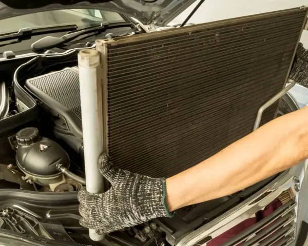 Mechanik w rękawicach wyjmuje chłodnicę klimatyzacji z silnika samochodu.