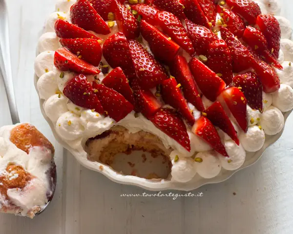 Delizioso tiramisù alle fragole, guarnito con panna montata, fragole fresche e pistacchi. Una fetta servita su un cucchiaio.