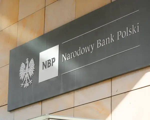 Tablica z godłem Polski i napisem "NBP Narodowy Bank Polski". Decyzje NBP wpływają na obniżkę stopy procentowej.
