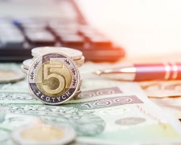 Złota moneta 5 złotych na stosie monet i banknotów. Obok długopis i kalkulator, sugerujące planowanie finansowe i możliwość recoverso rmc.