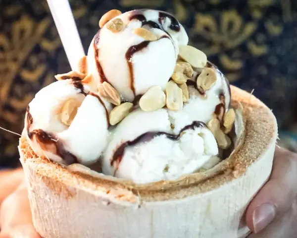 Cremiges Pina Colada Eis in einer Kokosnussschale, beträufelt mit Schokoladensauce und garniert mit Nüssen. Ein tropischer Genuss!