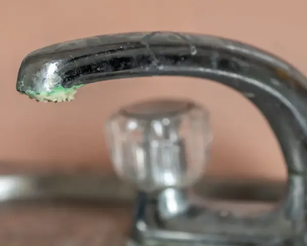 Robinet chromé avec un dépôt de calcaire vert de gris à son extrémité.