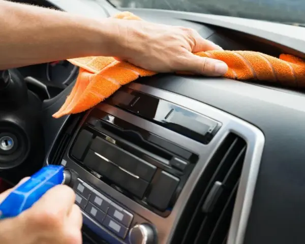 En hand sprayar och torkar av bilens instrumentbräda med en orange trasa. Det ser ut som en magisk rengöring för att få bilen skinande ren.