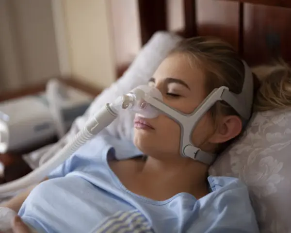 Kobieta śpi w masce CPAP, która pomaga w leczeniu bezdechu sennego. Urządzenie zapewnia ciągłe doprowadzanie powietrza, łagodząc objawy.