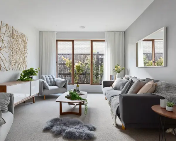 Sofá gris y sillón gris claro, con mesa de centro de madera. La decoración de ramas en la pared y la alfombra de piel gris crean un ambiente acogedor donde el beige y gris combinan a la perfección.