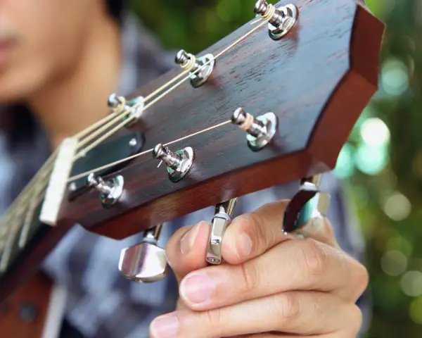 Nahaufnahme: Eine Hand stimmt eine 12-saitige Gitarre. Die Saiten sind gespannt, die Mechaniken glänzen.