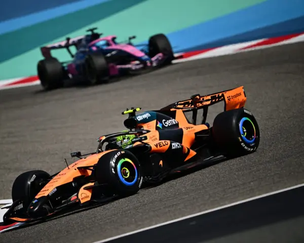 Un coche de Fórmula 1 naranja y negro compite en la pista, anticipando el reglamento F1 2026. Otro coche rosa y azul le sigue de cerca.