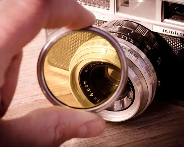 Une main tient un filtre protection objectif devant un vieil appareil photo argentique.