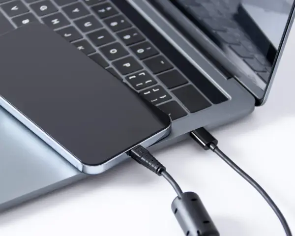 Ein iPhone wird über ein USB-C-Kabel mit einem Laptop verbunden, um Fotos zu übertragen.