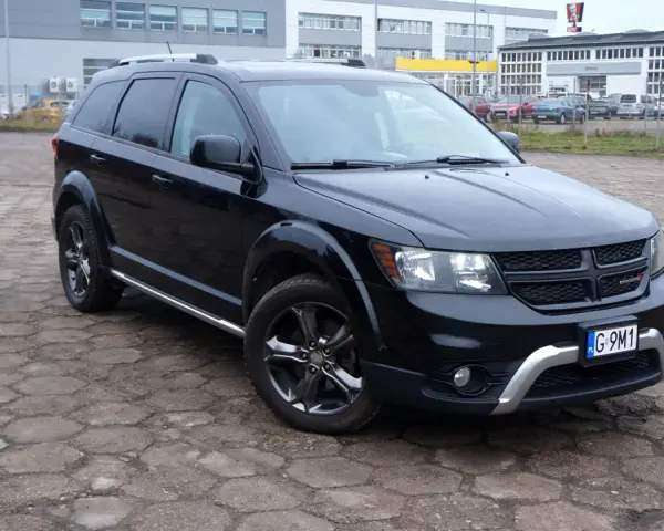 Czarny Dodge Journey 3.6 zaparkowany na placu z kostki brukowej. W tle budynki i inne samochody.