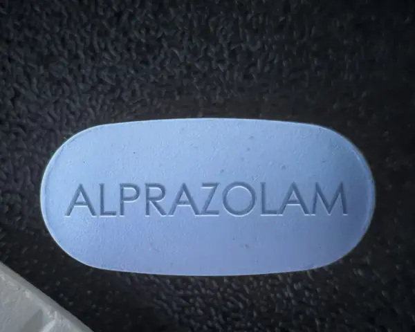 Niebieska tabletka z napisem "ALPRAZOLAM" leży obok białej. Uważaj na niebezpieczne skutki połączenia xanax i alkohol.
