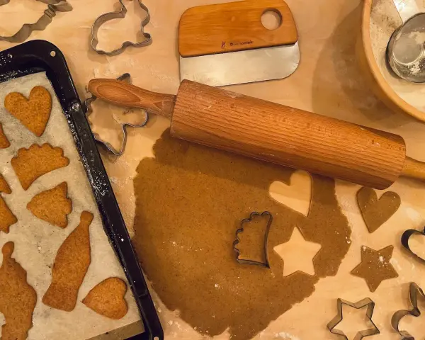 Pepparkaksdeg recept förbereds med kavel och pepparkaksformar. Färdiga pepparkakor ligger på en plåt.