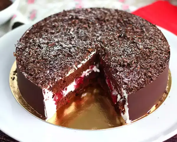 Tarta Selva Negra, con capas de bizcocho de chocolate, nata montada y cerezas, cubierta de virutas de chocolate y un toque de azúcar glas.