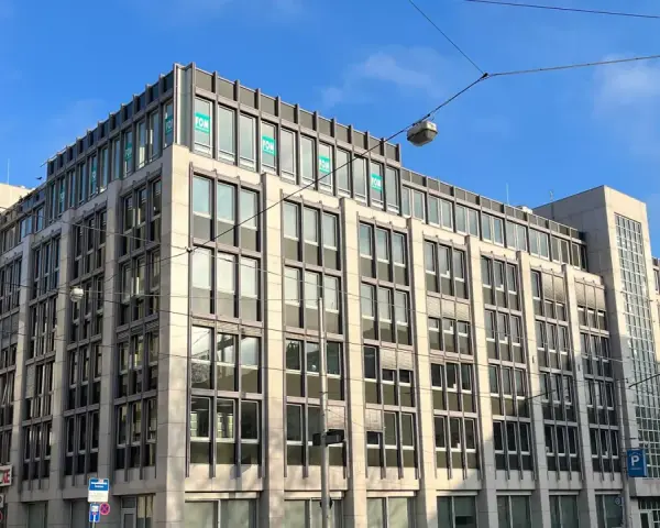 Modernes Bürogebäude in Kassel mit vielen Fenstern und "FOM"-Logos. Eine Apotheke ist im Erdgeschoss sichtbar.