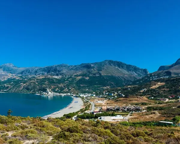 Malownicza zatoka z piaszczystą plażą i górami w tle. Urokliwe plaze Kreta zapraszają do odpoczynku.