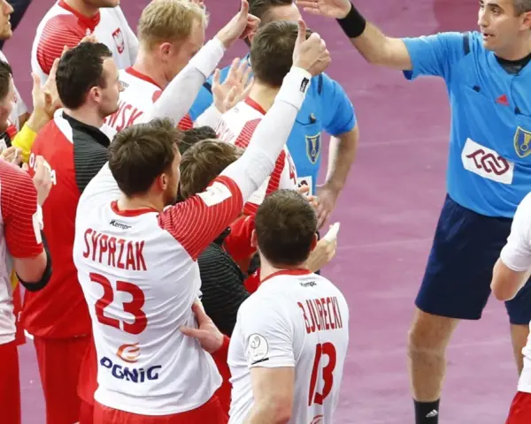 Polska kadra piłka ręczna świętuje zwycięstwo. Zawodnicy w białych strojach z czerwonymi detalami, z numerami 18, 23 i 15, cieszą się z sukcesu.