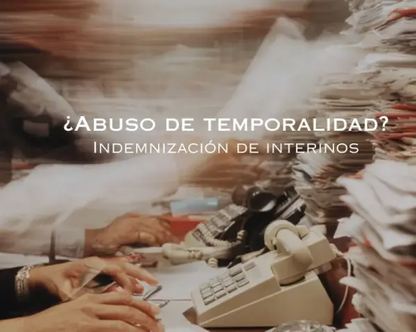 ¿Abuso de temporalidad? Indemnización de interinos tras 3 años. Escritorio caótico con papeles y teléfonos.