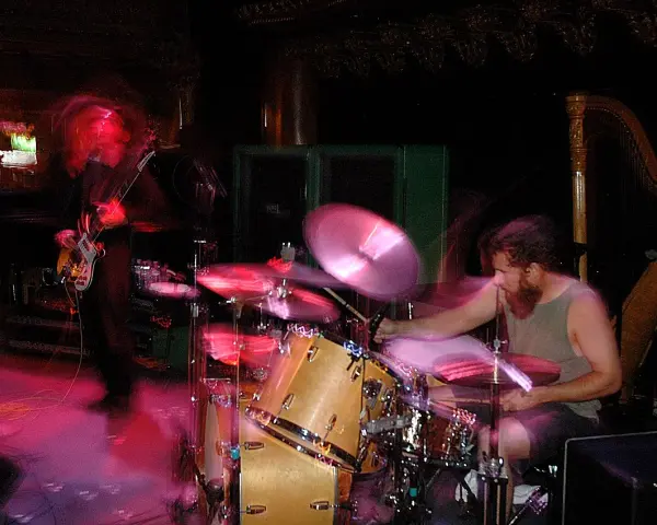 Ein Bassist und ein Schlagzeuger einer Stoner Rock Band in Aktion. Die Lichter und Bewegungen erzeugen eine dynamische Atmosphäre.