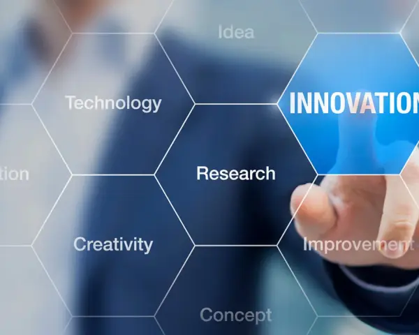 Dłoń dotyka ekranu z napisem "INNOVATION", otoczonego przez sześciokąty z hasłami: Idea, Technology, Research, Creativity, Invention, Improvement. To wizualizacja procesu, który może być częścią wzornictwo przemysłowe studia.