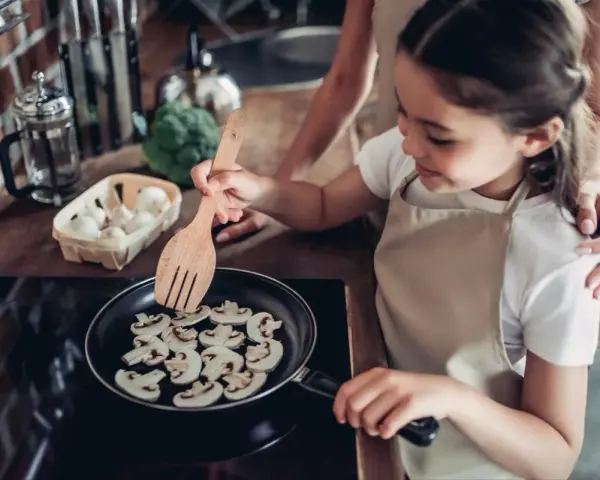 Mała kucharka smaży pieczarki na patelni. Czy dzieci mogą jeść pieczarki? Tak, to zdrowy dodatek do posiłków!