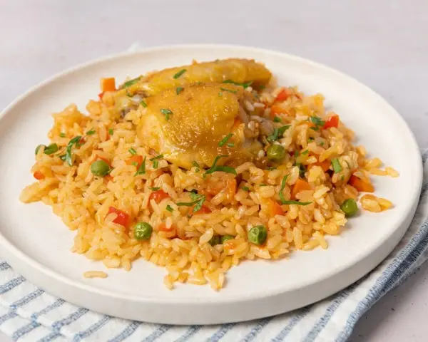 Arroz con pollo jugoso con verduras y perejil picado en un plato blanco.
