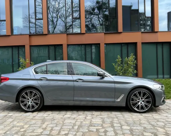 Szary sedan BMW G30 na tle nowoczesnego budynku.