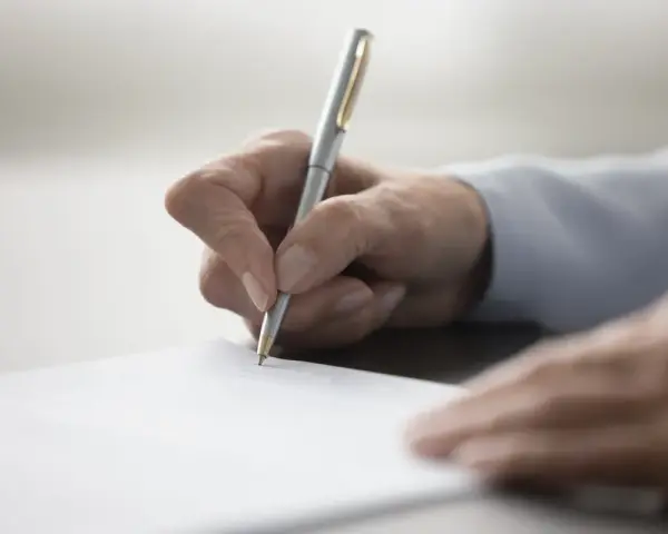 Dłoń testamentora pisze długopisem na dokumencie.