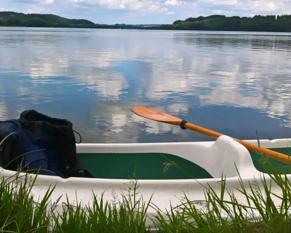 Wiosło i plecak w łodzi na spokojnym jeziorze raduńskim dolnym. Chmury odbijają się w tafli wody.