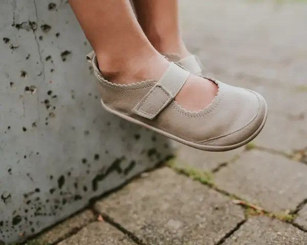 Małe stópki w beżowych balerinach z gumką, siedzące na betonowym murku.