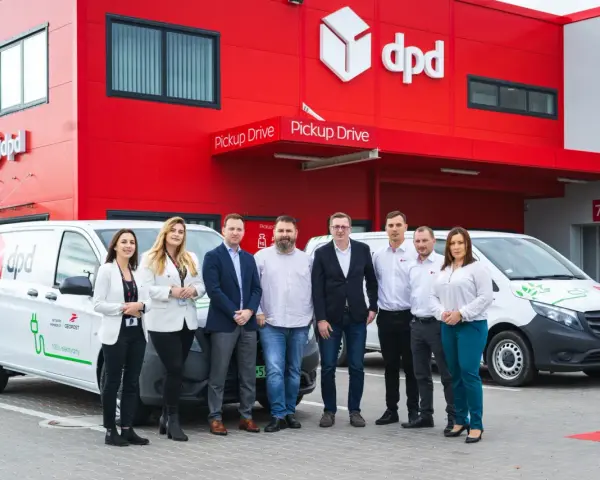 Zespół DPD pozuje przed budynkiem z logo firmy i elektrycznym dpd bus.